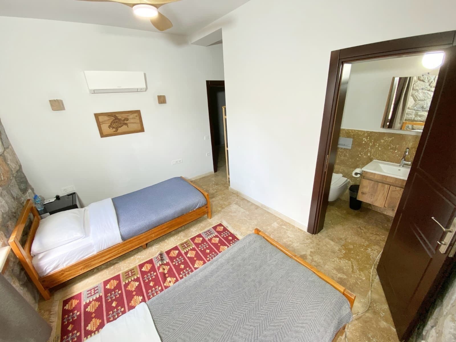 Ein kleiner, kompakter Raum mit einem Bett, einer Sitzbank, einem Spiegel und einem Badezimmer mit Waschbecken.