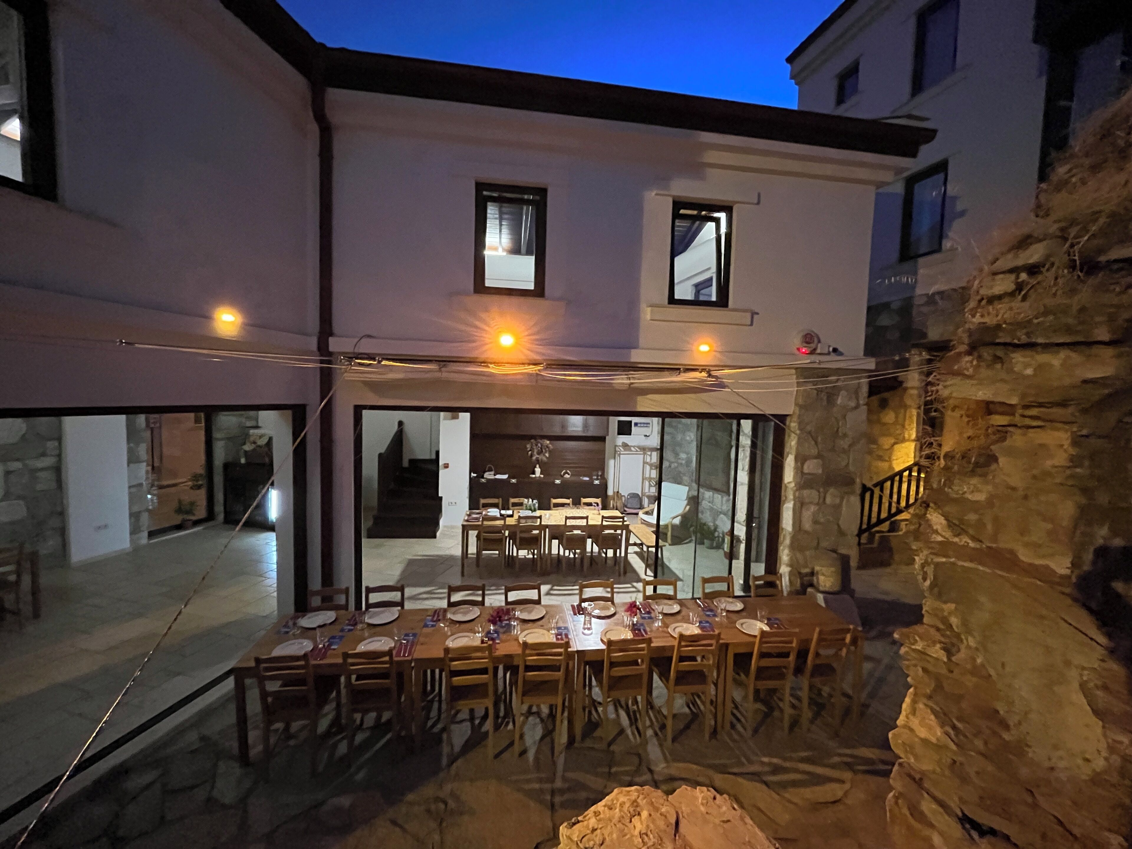 An outdoor dining area with a long table set for a meal, surrounded by stone walls and a glass enclosure.
