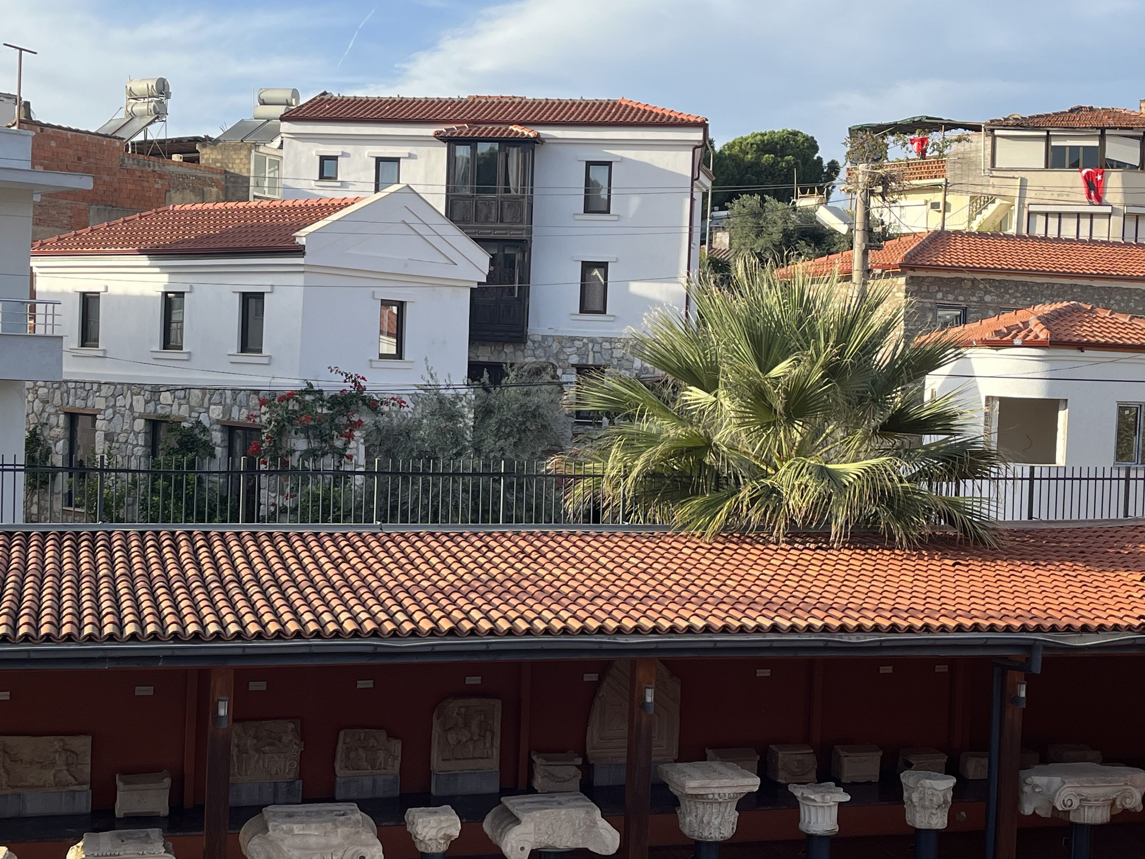 A building with a red-tiled roof, white walls, and a palm tree in the foreground.
