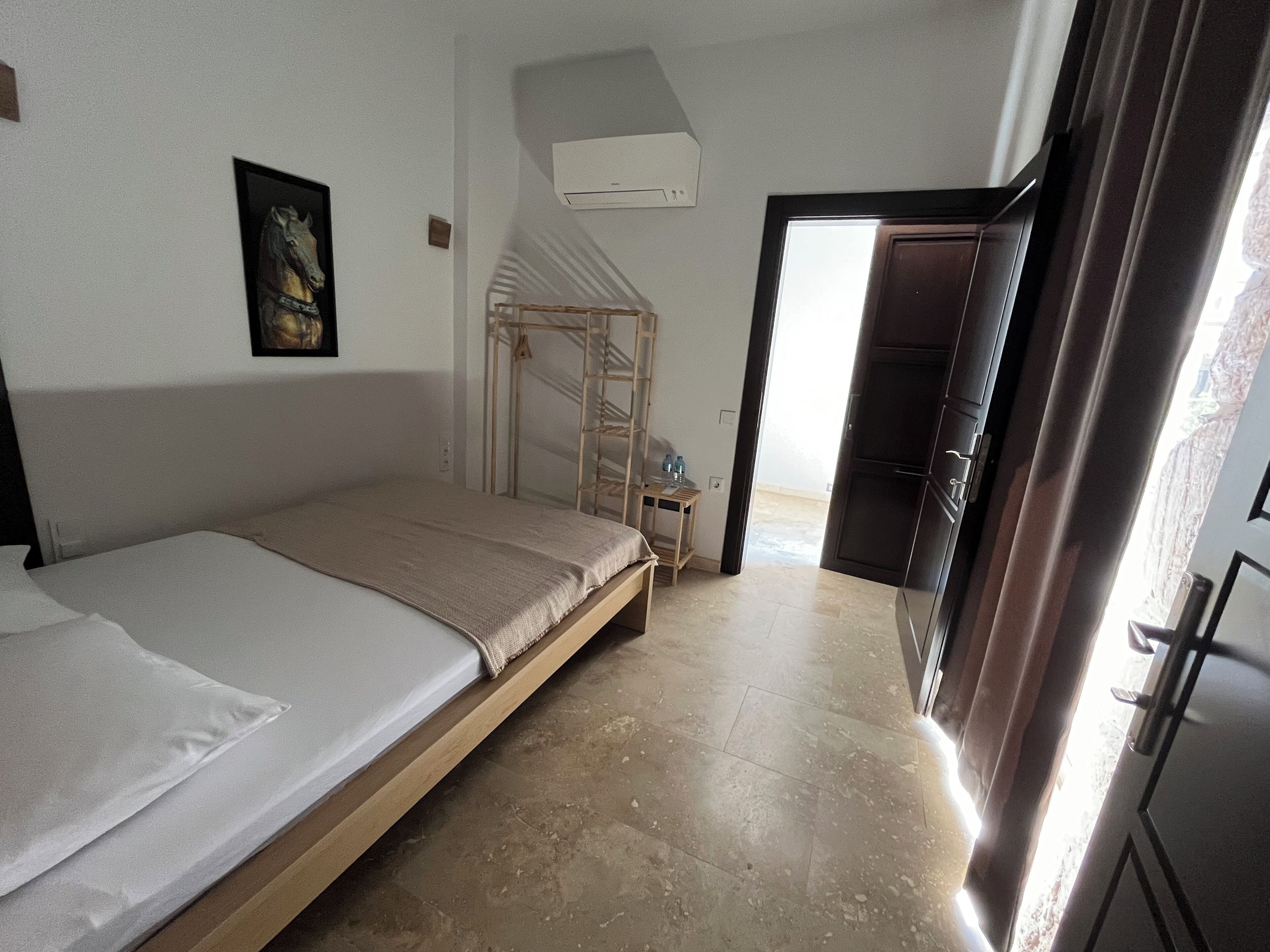 A bedroom with a bed, a wooden ladder, an air conditioning unit, and a door leading to another room.