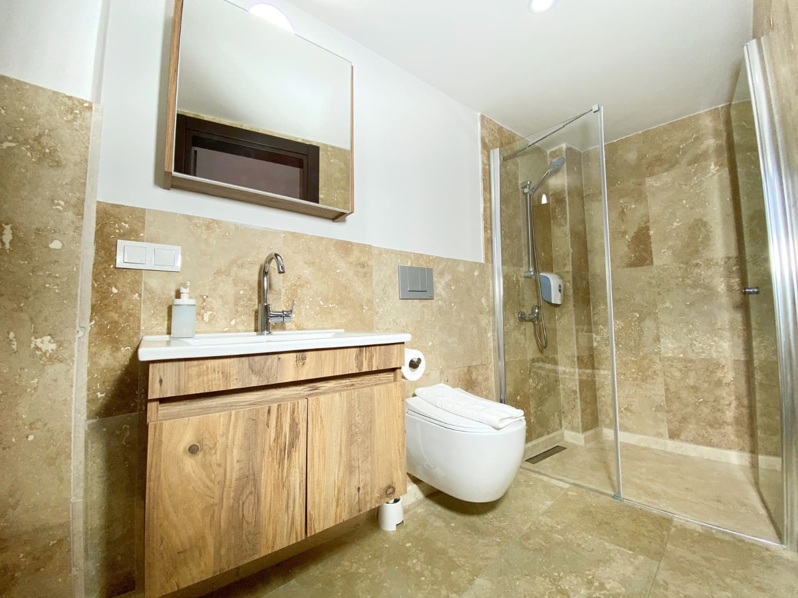 Une salle de bain avec un meuble-lavabo en bois, un lavabo blanc, un miroir, des toilettes et une cabine de douche en verre.