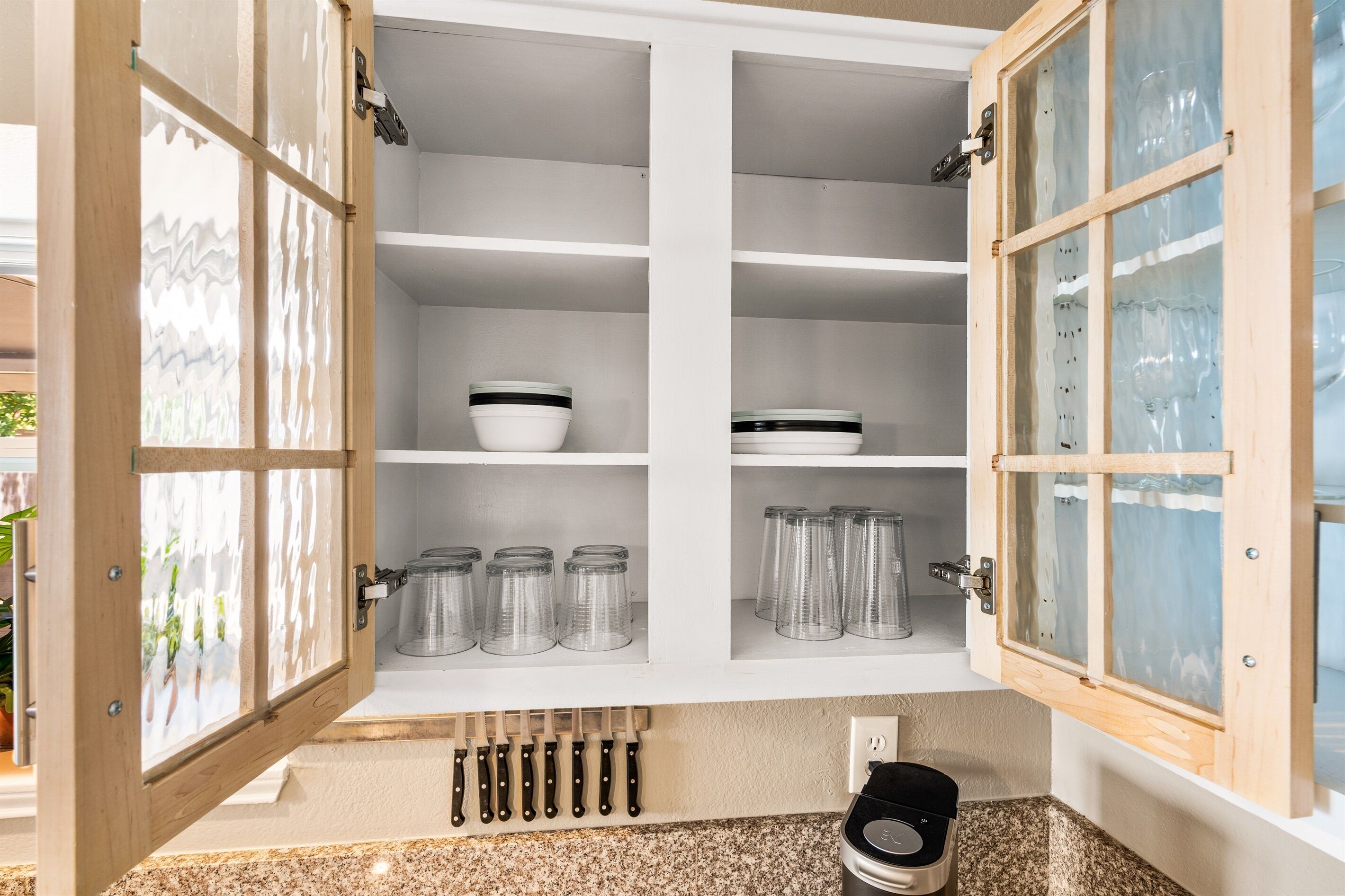 A kitchen with open cabinets containing glassware, bowls, and utensils.