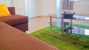 A living room with a brown sofa, a glass coffee table, and a green rug. - Airport Lounge - 3Bed 6 Persons (Manchester)
