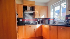 A kitchen with wooden cabinets, a gas stove, a microwave, and a window with a view of the outside. - Airport Lounge - 3Bed 6 Persons (Manchester)
