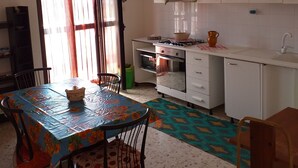 A compact kitchen with white cabinets, a gas stove, and a sink. There is a dining table with chairs and a window with curtains.