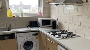 Une cuisine compacte équipée d’un lave-linge, d’un four à micro-ondes, d’une cuisinière à gaz et de meubles de rangement en bois.