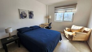 Un dormitorio con cama, escritorio, silla, lámpara y cuadros en la pared.
