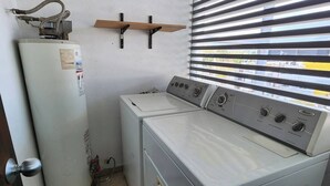 Un lavadero con lavadora, secadora, calentador de agua y una ventana con persianas.
