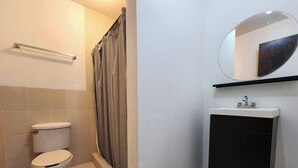 Un baño con inodoro, cortina de ducha, lavamanos con espejo y toallero.