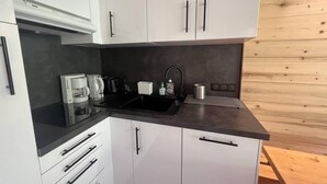 A modern kitchen with white cabinets, a black countertop, and a wooden wall. - 20m from ski slopes, 1st floor, view ski slopes, terrace, ski locker, 27m², Méribel-Mottaret (Méribel - Les Allues)