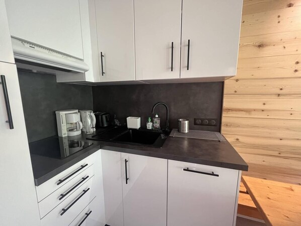 A modern kitchen with white cabinets, a black countertop, and a wooden wall.