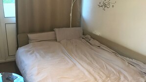 Ett enkelrum med en utdragbar låda, ett sängbord med en telefon och ett fönster med gardiner.