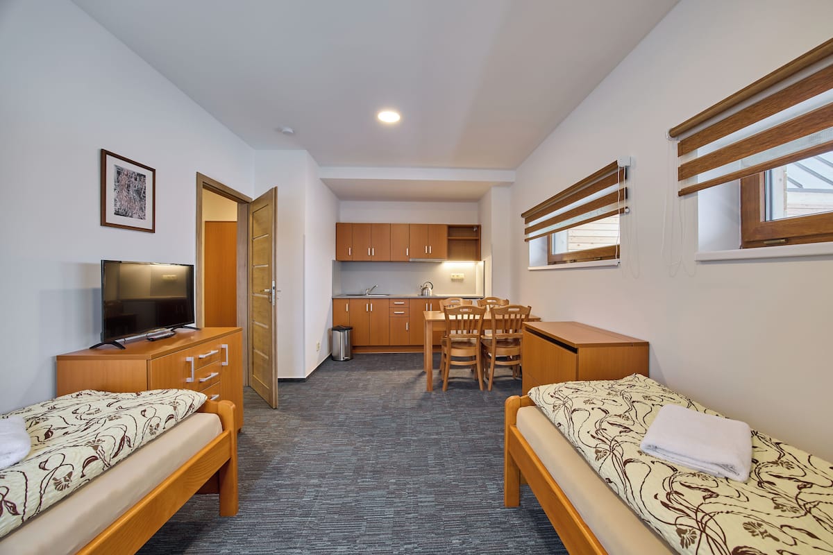 A compact room with two single beds, a small kitchenette, a dining table, and a TV.