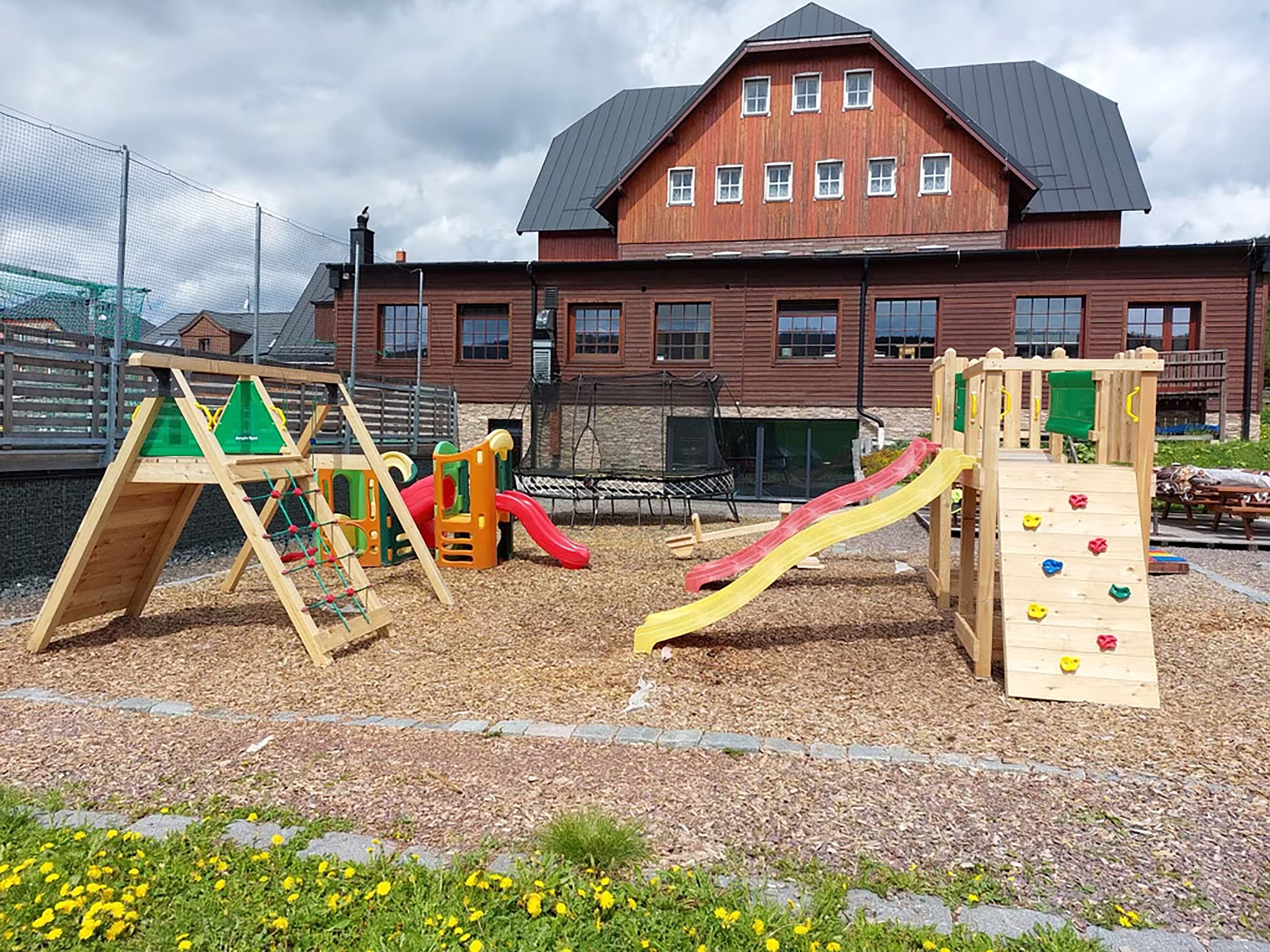A playground with climbing structures and slides, surrounded by a playground area with mulch and flowers.