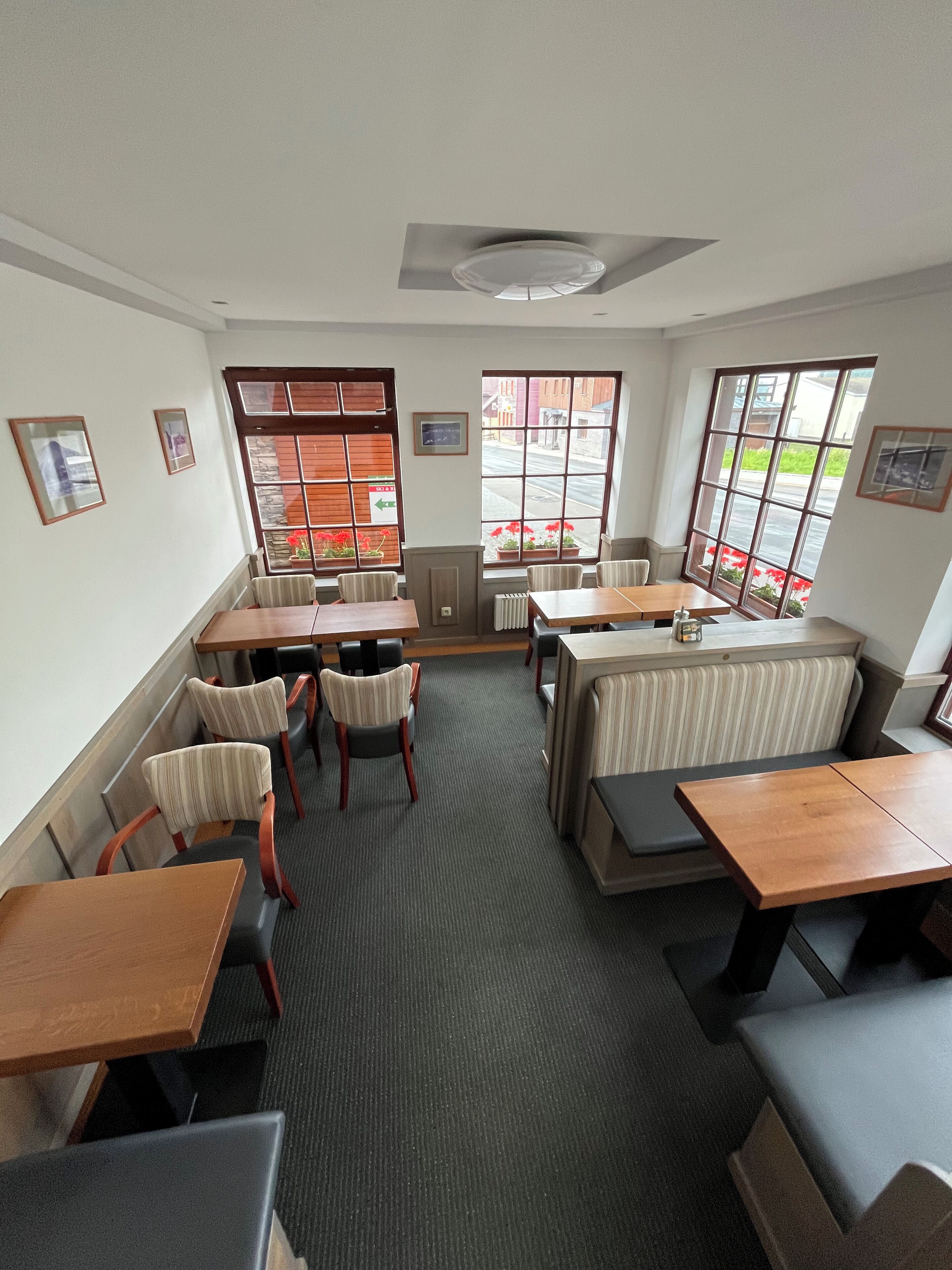 A restaurant with booths and tables, large windows with views of the street, and framed pictures on the walls.