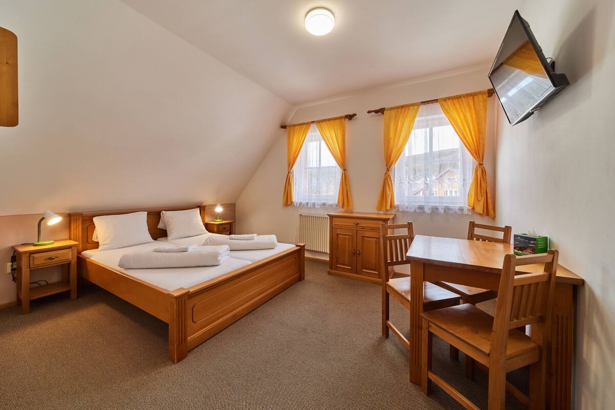 A bedroom with a wooden bed, bedside tables, a desk, chairs, and a TV mounted on the wall.