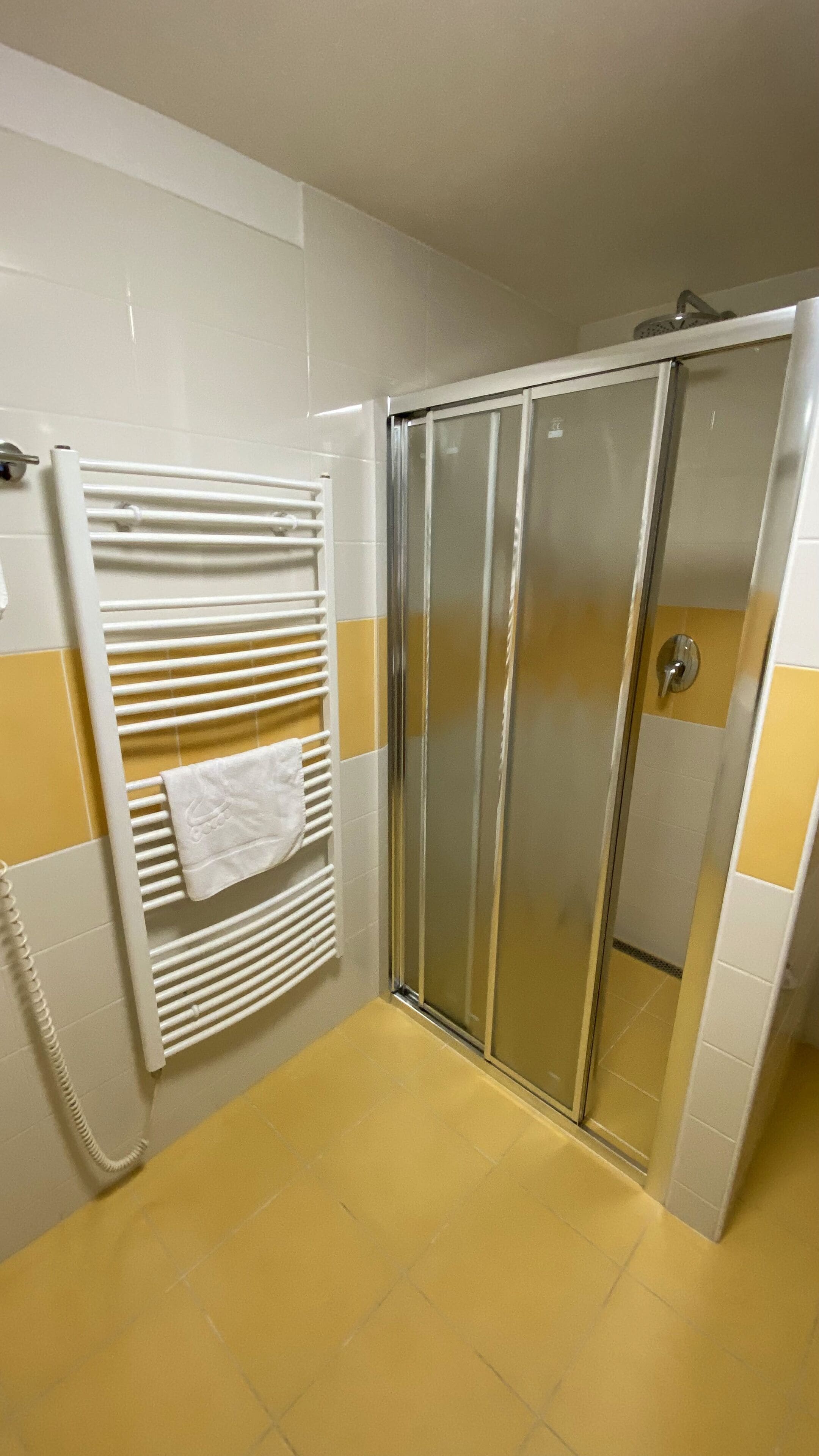 A bathroom with a glass shower door, a towel rack with a white towel, and yellow-tiled walls.