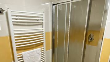 A bathroom with a glass shower door, a towel rack with a white towel, and yellow-tiled walls.
