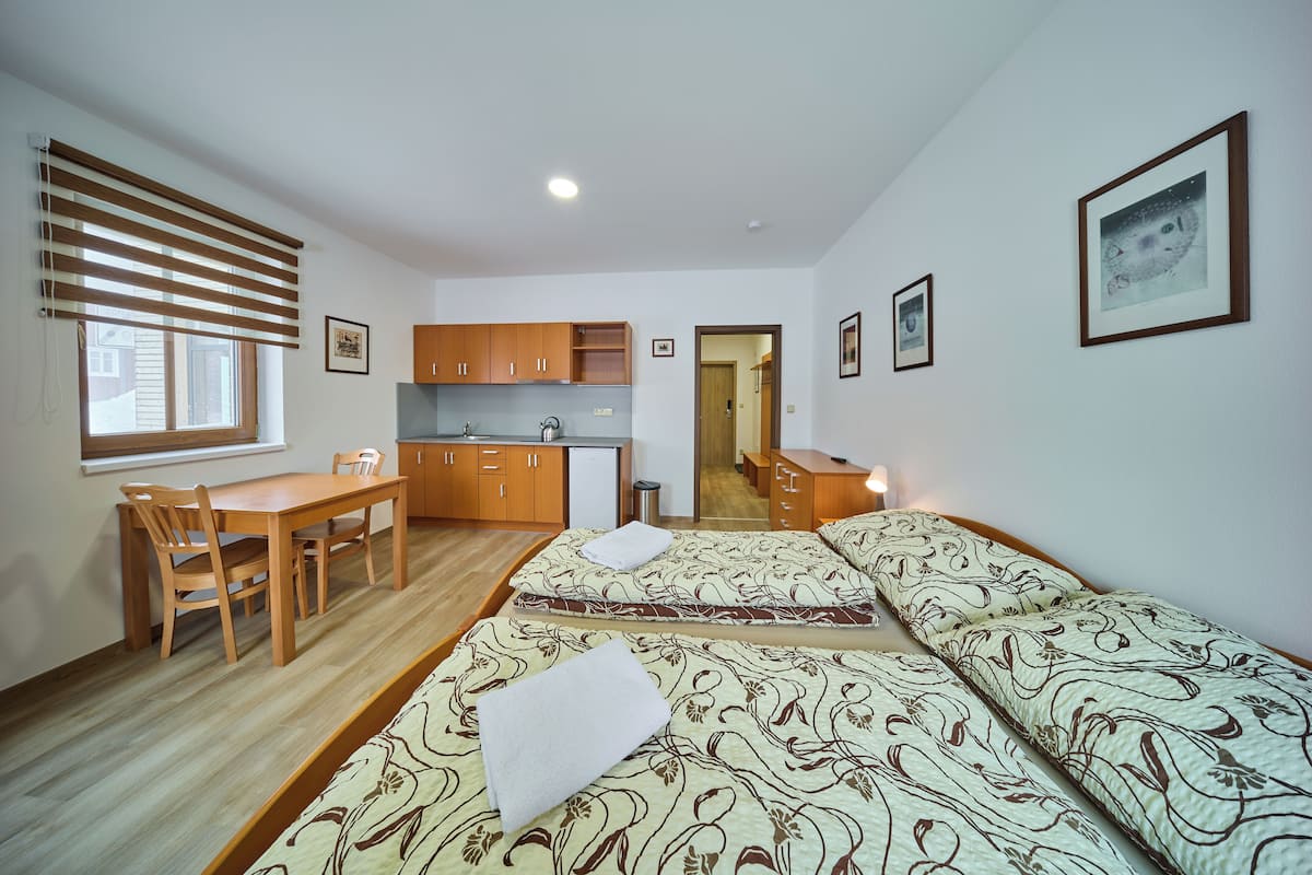 A compact hotel room with a kitchenette, a dining area, and two beds with floral-patterned bedding.