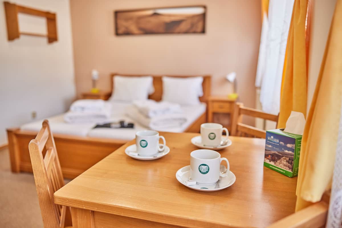 A hotel room with a wooden bed, a wooden table with two white cups and saucers, a box of tea, and a painting on the wall.
