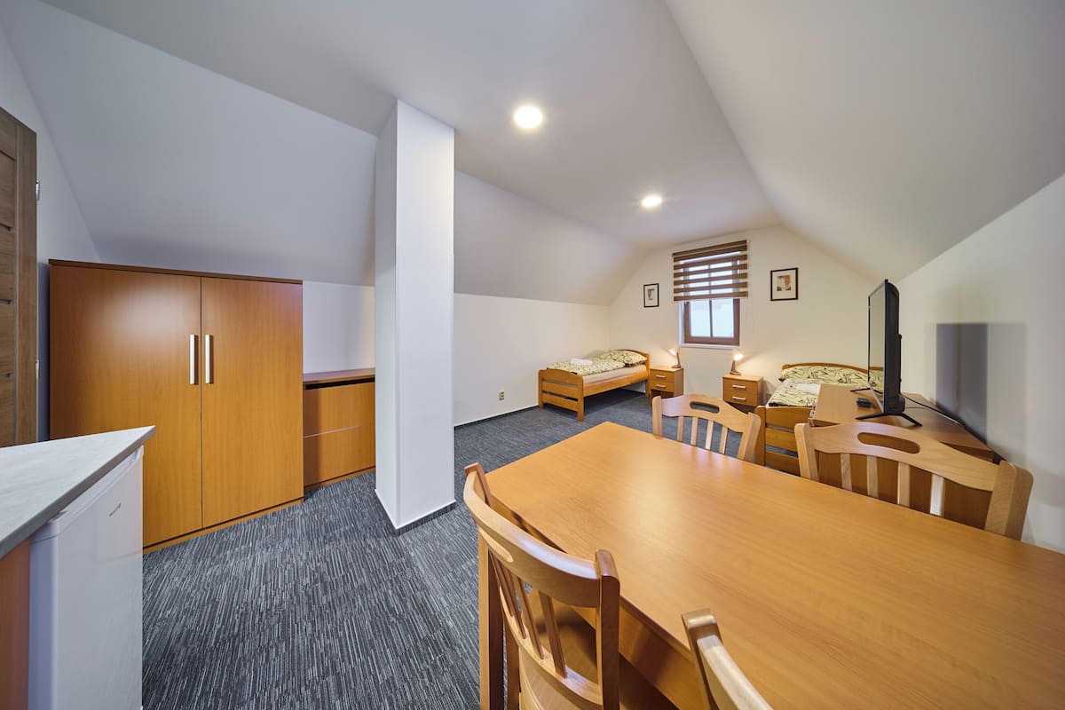 A compact room with a wooden dining table, a bed with a patterned bedspread, a small desk, and a wardrobe.