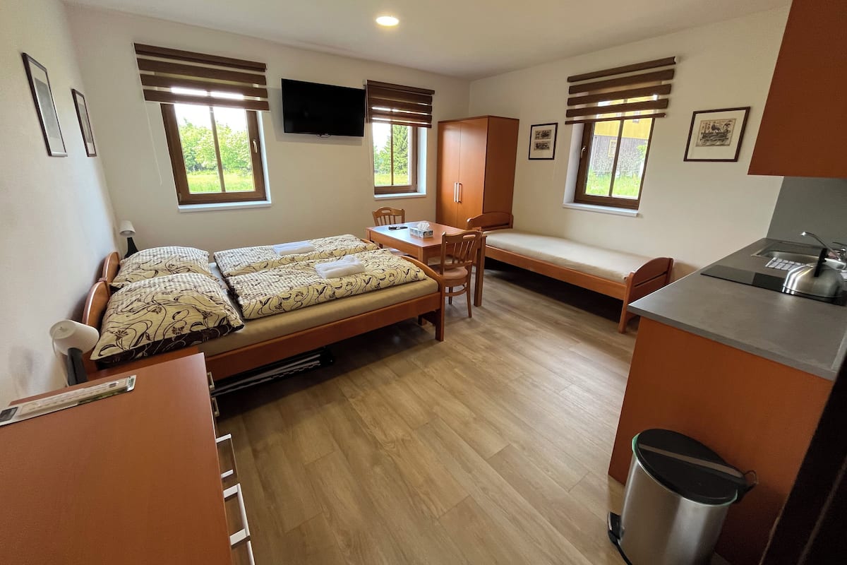 A compact room with two beds, a desk, a chair, and a small kitchenette.