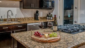 A kitchen with granite countertops, dark cabinets, a stainless steel range hood, and a wine bottle on the counter. - The Oasis - Heated Pool - Spa - Arcade (Scottsdale)