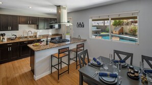 A modern kitchen with dark cabinets, a granite countertop, and a dining area with a pool view. - The Oasis - Heated Pool - Spa - Arcade (Scottsdale)
