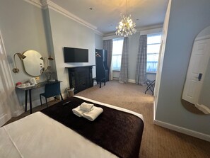 A hotel room with a large bed, a flat-screen TV, a fireplace, a desk with a chair, and a window with curtains. - Arran House Hotel (London)