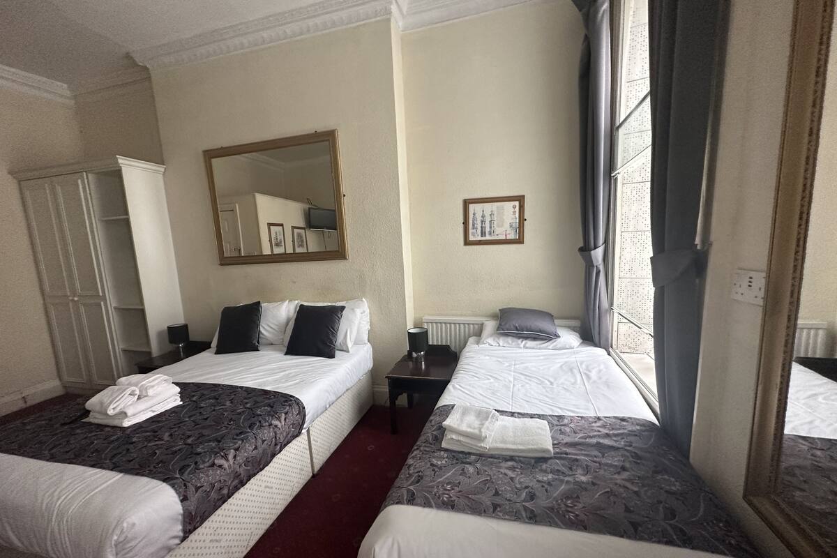 A hotel room with two beds, a wardrobe, a mirror, a framed picture, and a window with curtains.