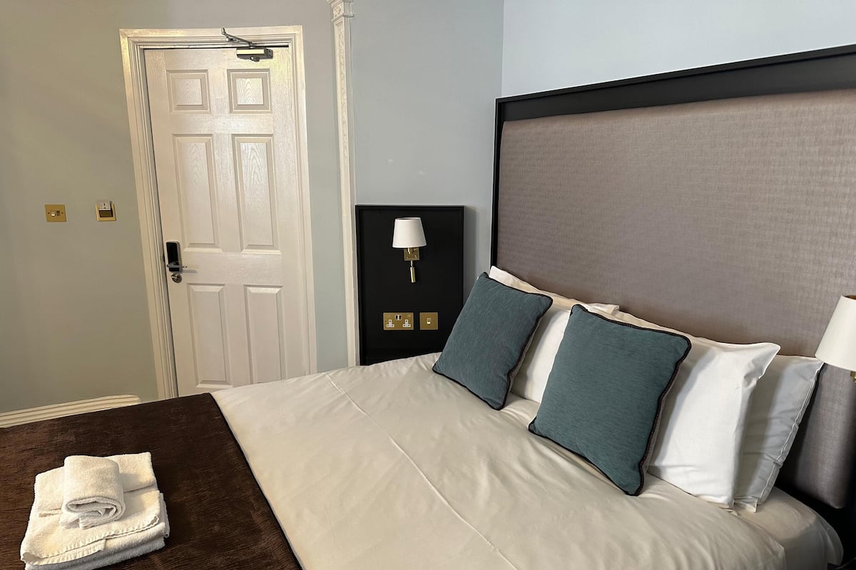 A neatly made bed with white and teal pillows, a dark headboard, and a folded towel on the side.