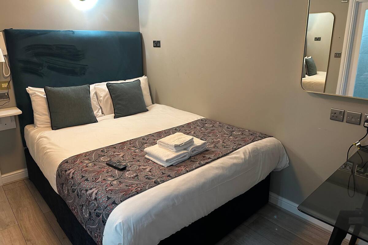 A neatly made bed with a patterned bedspread, a remote control, and a folded towel on the bed.