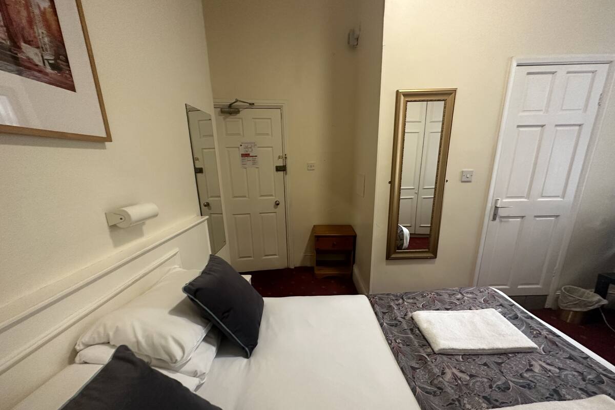 A hotel room with a bed, pillows, a bedside table, a mirror, and a door.