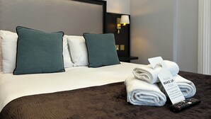 Een net opgemaakt bed met witte en teal kussens, een opgevouwen handdoek en een afstandsbediening op een donkerbruin hoofdbord.