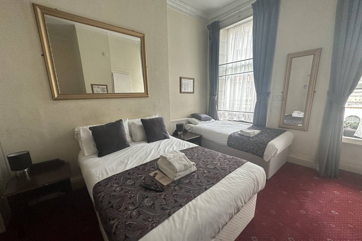 A hotel room with two beds, a large mirror, a window with curtains, and a red carpet.