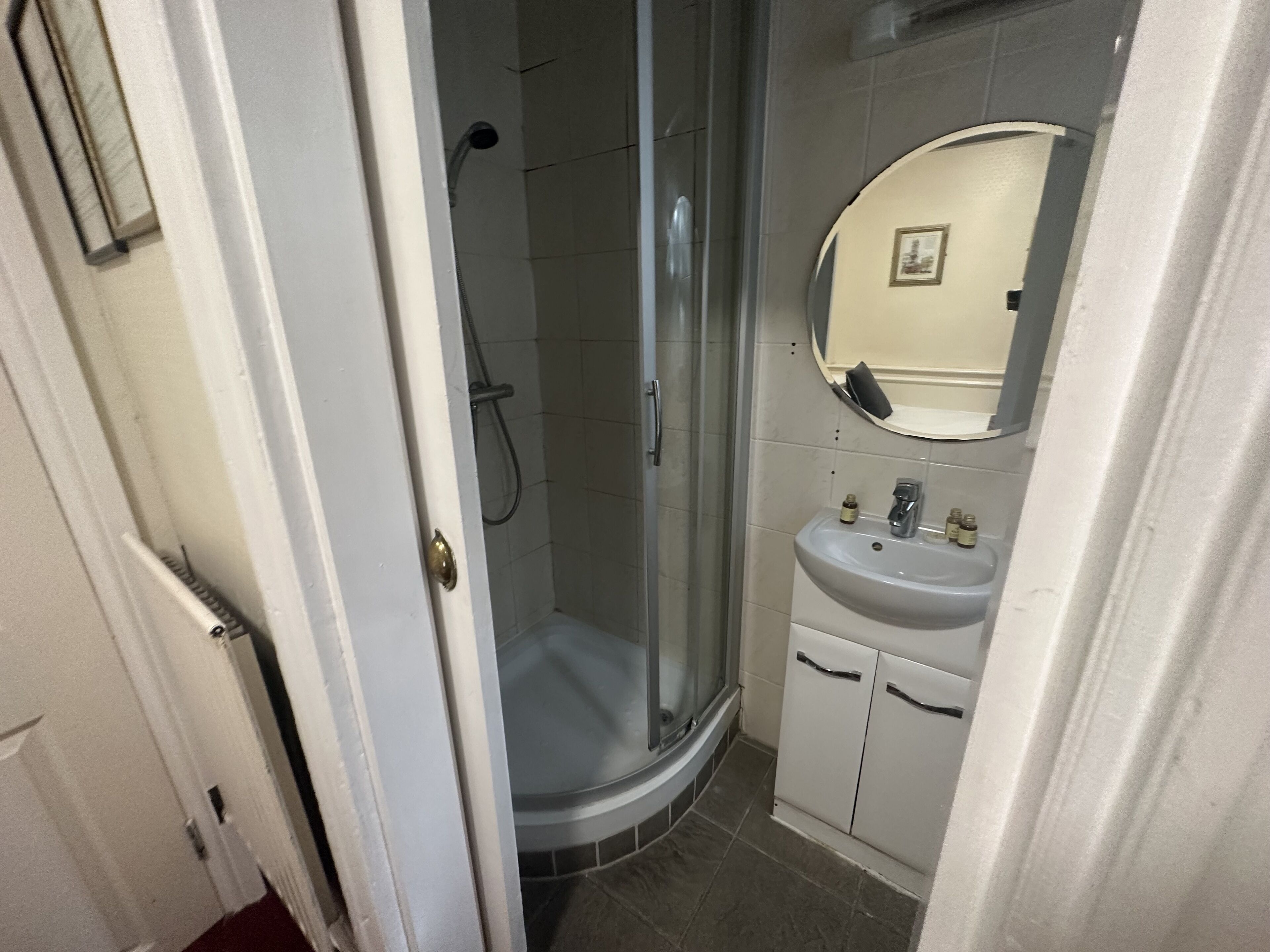 A bathroom with a glass-enclosed shower, a sink with a mirror above it, and a cabinet below.