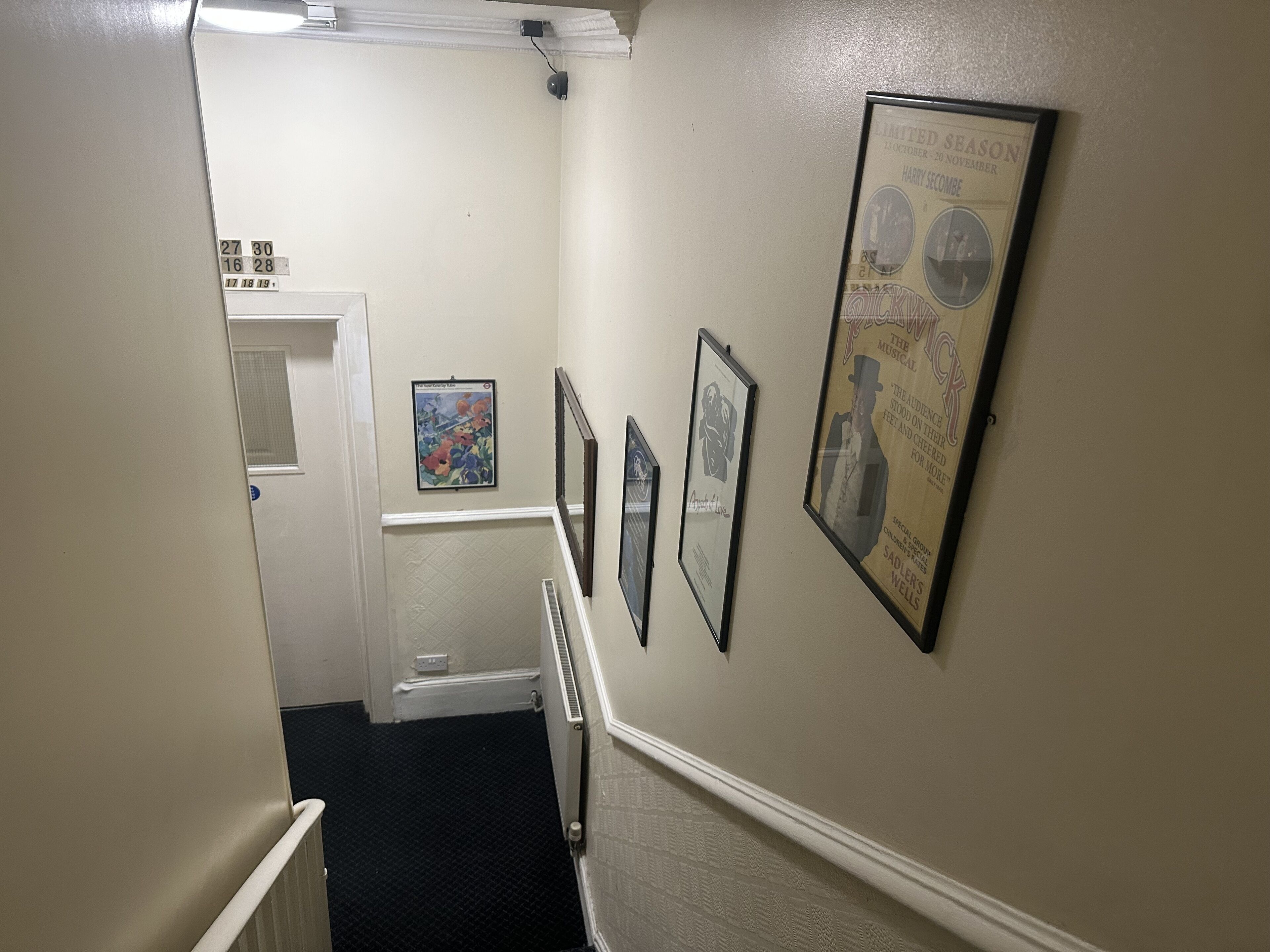 A hallway with framed posters on the walls, a door at the end, and a radiator along the wall.