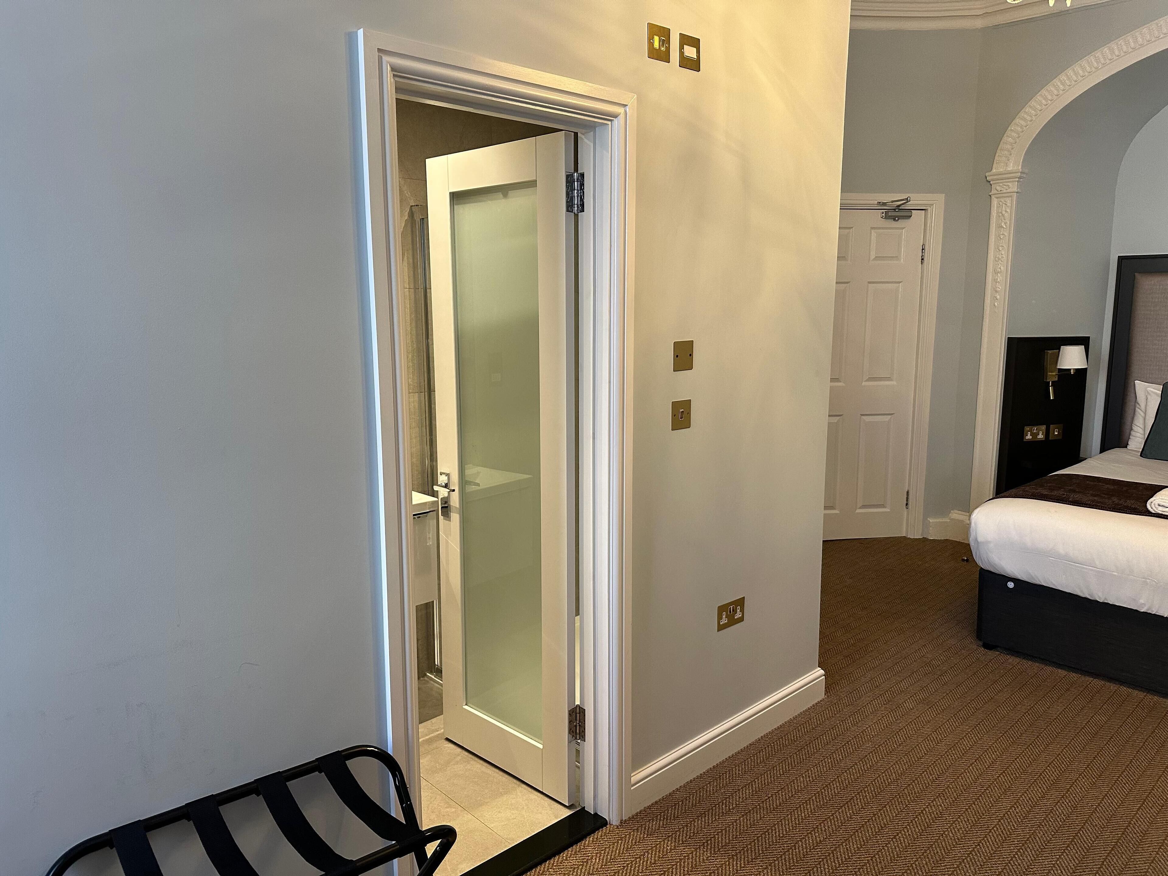 A hotel room with a bed, a chair, a door leading to a bathroom, and a carpeted floor.