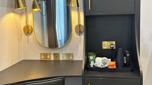 Een moderne hotelkamer met een donkergrijze kast, een ronde spiegel met gouden details, een zwart bureau en een zwarte stoel.
