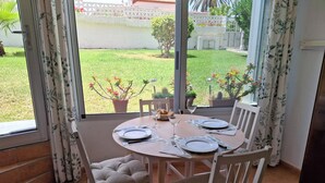 A dining area with a table set for four, white chairs, and a view of a garden through large windows.