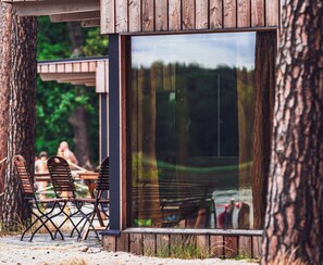 A wooden outdoor seating area with metal chairs and a table, surrounded by trees. - Naturcamping Brettmühlenteich e.G. (Thiendorf)