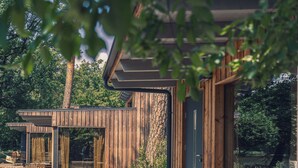 A wooden cabin with a patio area featuring two chairs and a table. - Naturcamping Brettmühlenteich e.G. (Thiendorf)