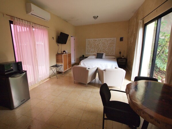 A hotel room with a bed, a desk, a chair, a TV, and a window with a view of greenery.