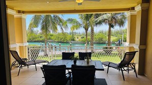 Une terrasse couverte, avec une table et des chaises, donnant sur une piscine et un espace verdoyant.