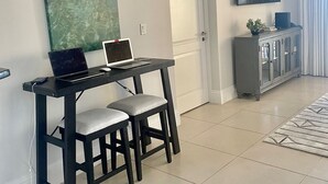 Un salon moderne avec un bureau en bois foncé, deux fauteuils gris rembourrés, une grande peinture abstraite, un téléviseur à écran plat fixé au mur et un meuble gris avec des portes en verre.