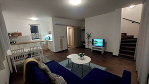 A modern living room with a sofa, a coffee table, and a TV. There is a staircase leading to another level. - Vitorlás apartman 2
 (Balatonszárszó)