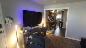 A living room with a flat-screen TV, a wooden entertainment unit, and a dining area visible through an open doorway. - Aurora on the Medical Mile - Crisp Cozy Certified - Extended stay friendly (Grand Rapids)