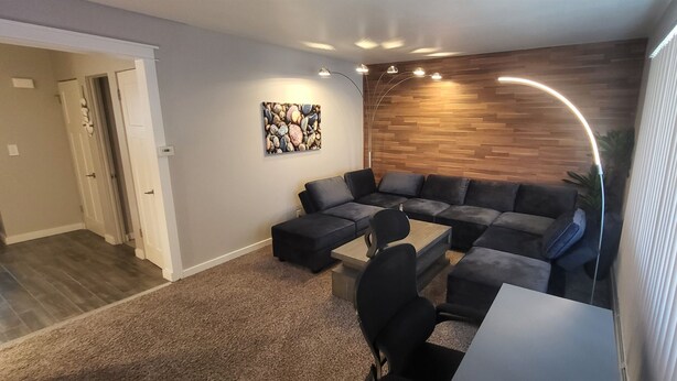 A modern living room with a sectional sofa, a coffee table, and a painting on the wall. - Aurora on the Medical Mile - Crisp Cozy Certified - Extended stay friendly (Grand Rapids)