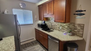 A compact kitchen with wooden cabinets, a stainless steel refrigerator, a microwave, and a sink. - Aurora on the Medical Mile - Crisp Cozy Certified - Extended stay friendly (Grand Rapids)
