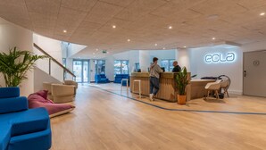 Un área de recepción moderna con suelo de madera, asientos azules y rosados, y un mostrador de recepción.